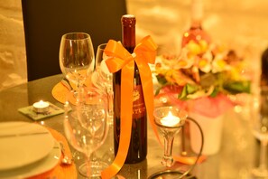 Uma mesa posta com taças de vinho, uma garrafa, uma vela e um pequeno vaso com flores.