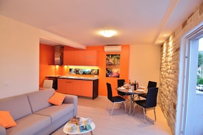 A modern living room with a sofa, a dining table set for two, and a kitchen area with orange cabinetry. - Welcoming 1-bedroom apartment with AC in Dubrovnik with private parking place (Dubrovnik)