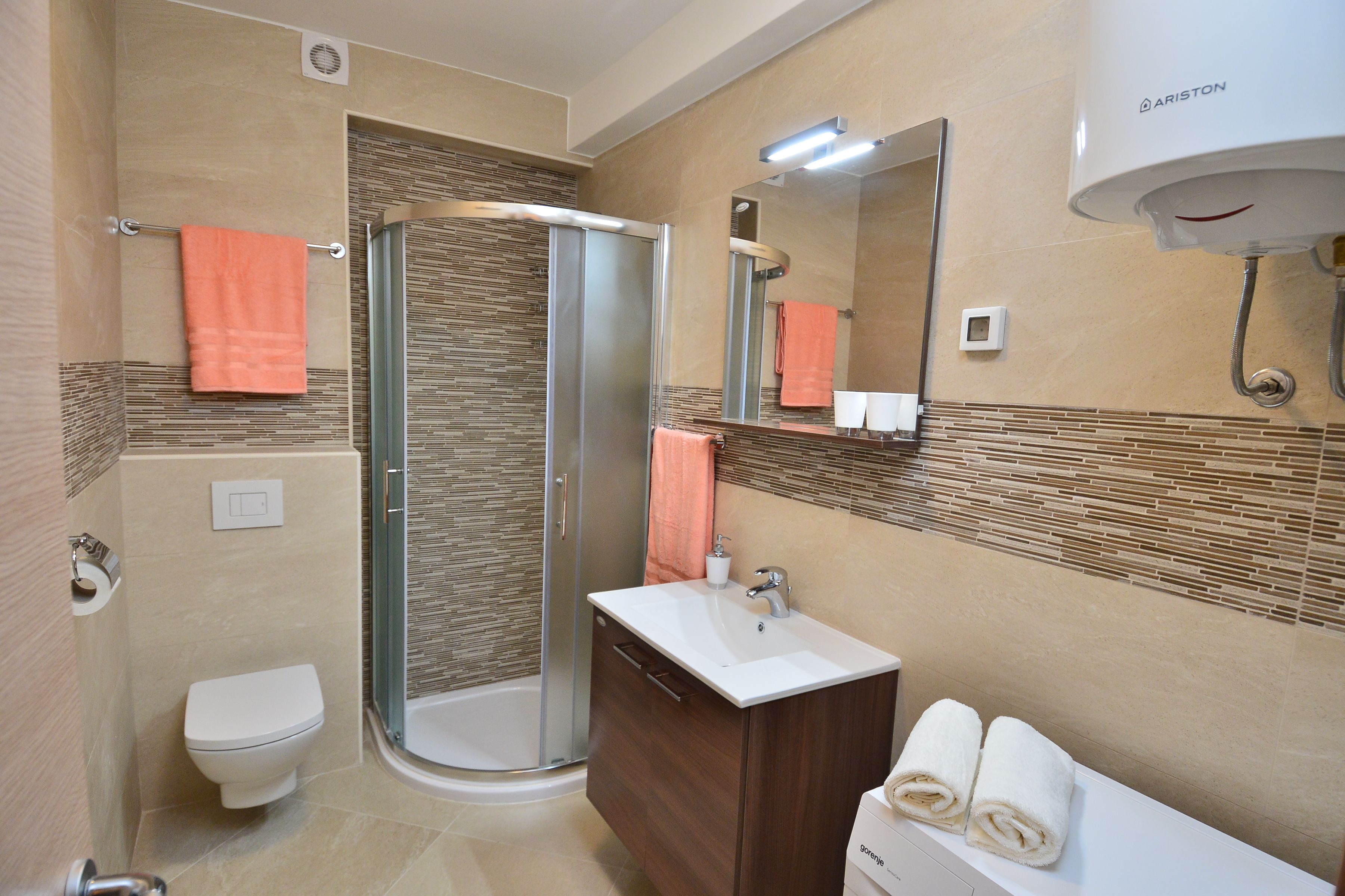 A modern bathroom with a glass-enclosed shower, a toilet, a sink with a mirror above, and a towel rack with towels.