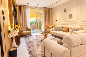 A spacious living room with a beige sofa set, a glass coffee table, and a large sliding glass door leading to an outdoor area. - Hotel Apartment 10 minutes away from The Airport (Cairo Governorate)