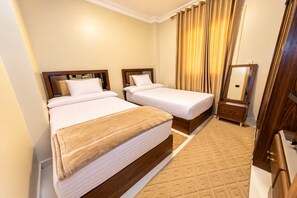 Ein Hotelzimmer mit zwei Betten, einem Holzkopfstück, einem kleinen Nachttisch, einem Spiegel und einem gemusterten Teppich.