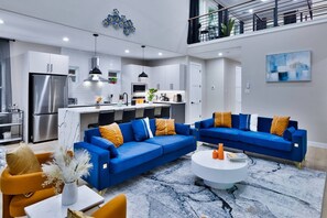 A modern living room with a blue sectional sofa, a white coffee table, and a kitchen area with stainless steel appliances. - Luxe Living in the heart of Dallas (Dallas)