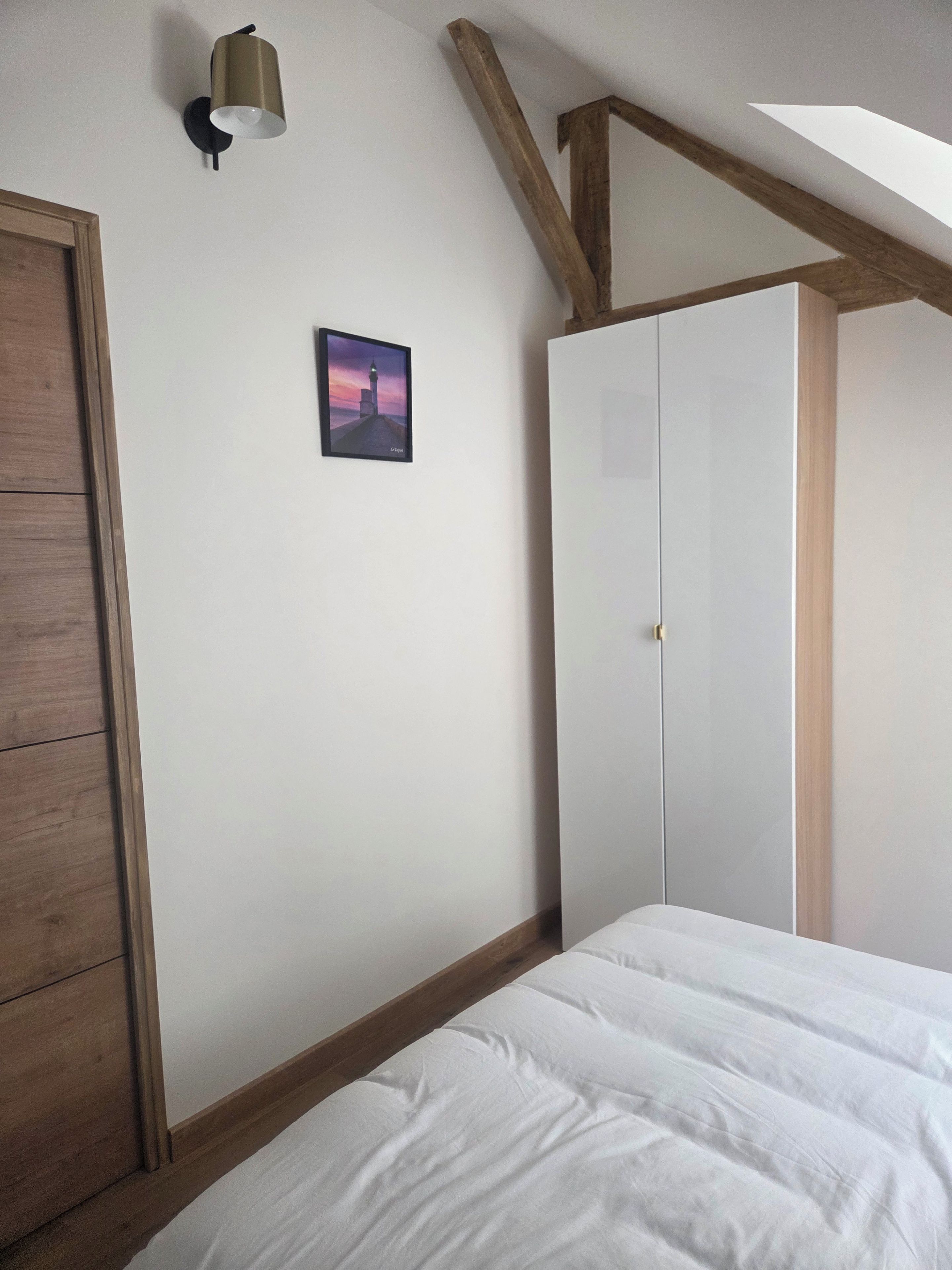 Een slaapkamer met een bed, een kledingkast, een schilderij aan de muur en een dakraam.