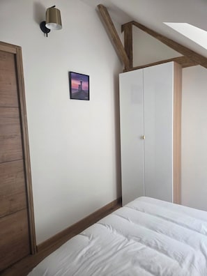 Quarto com cama, guarda-roupa, um quadro na parede e um clarabóia.