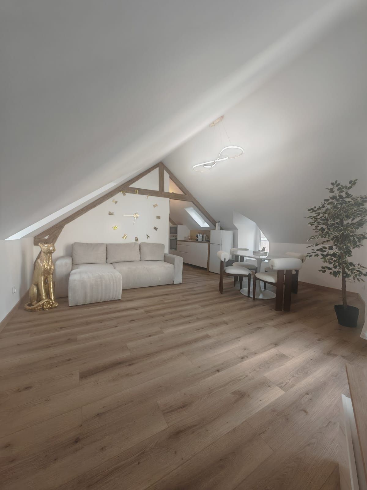 Een loft-achtige kamer met een schuine plafond, een bank, een eettafel en een potplant.