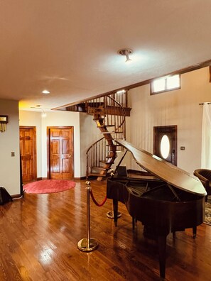 A spacious room with a grand piano, a wooden staircase, and a red carpet. - Elegant 5,000 Sq Ft Estate on 3 Acres, Pool&Jacuzzi. 10 min from Downtown Indy! (Indianapolis)