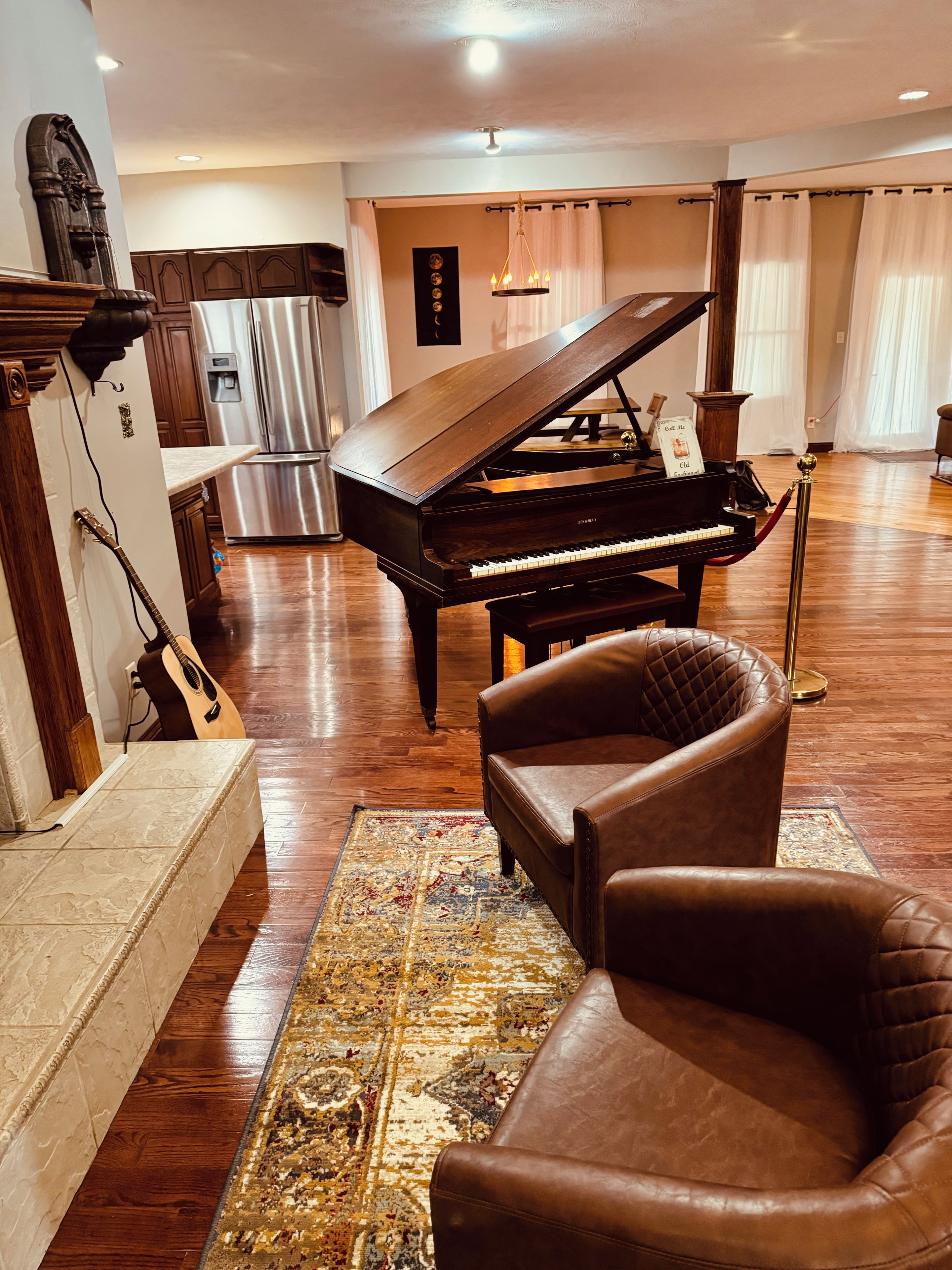 A grand piano in a spacious room with a wooden floor, a leather armchair, and a rug.