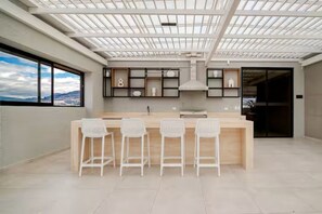 A modern kitchen with a central island, bar stools, and a view through a large window. - Stylish Suite in La Carolina, Parking + Gym (Quito)