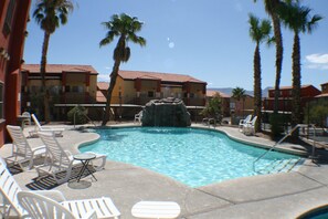 A swimming pool with lounge chairs and palm trees, surrounded by buildings with red-tiled roofs. - Cozy 2-bedroom condo with AC in perfect Mesquite (Mesquite)