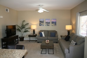 A living room with a television, two couches, a coffee table, a plant, and a ceiling fan. - Cozy 2-bedroom condo with AC in perfect Mesquite (Mesquite)