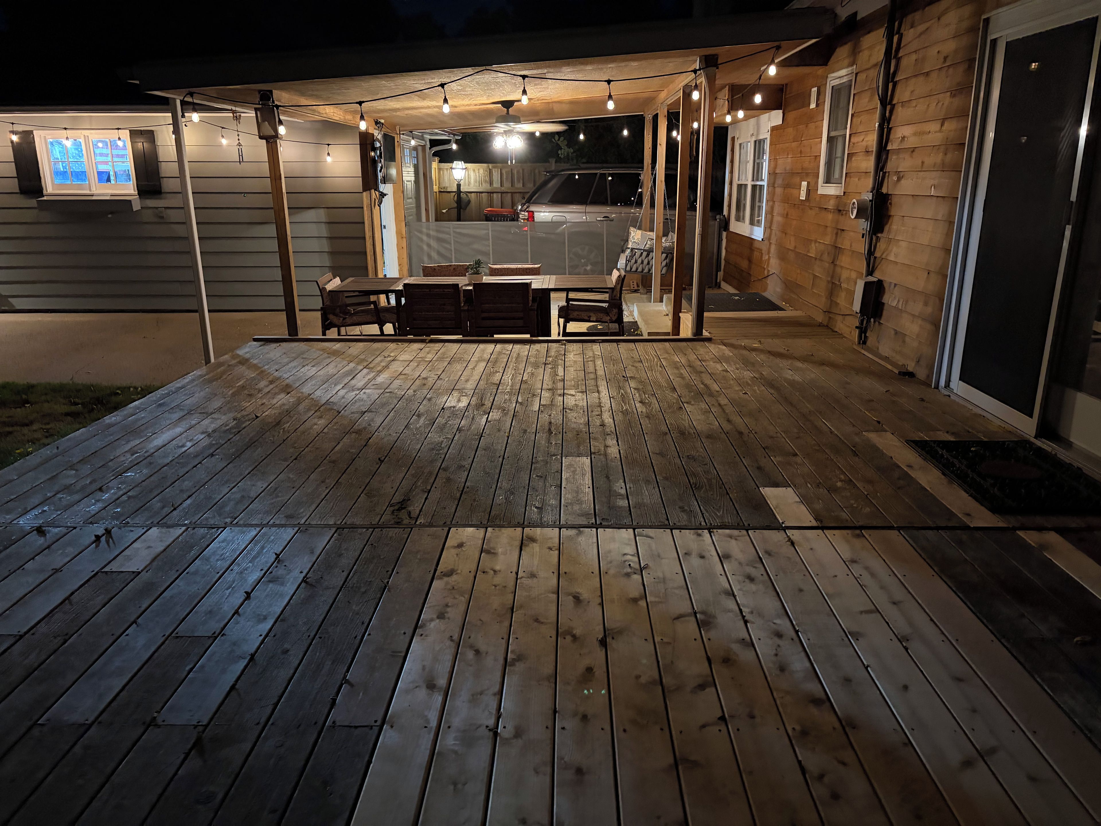 A wooden deck with string lights, a covered seating area, and a garage entrance.