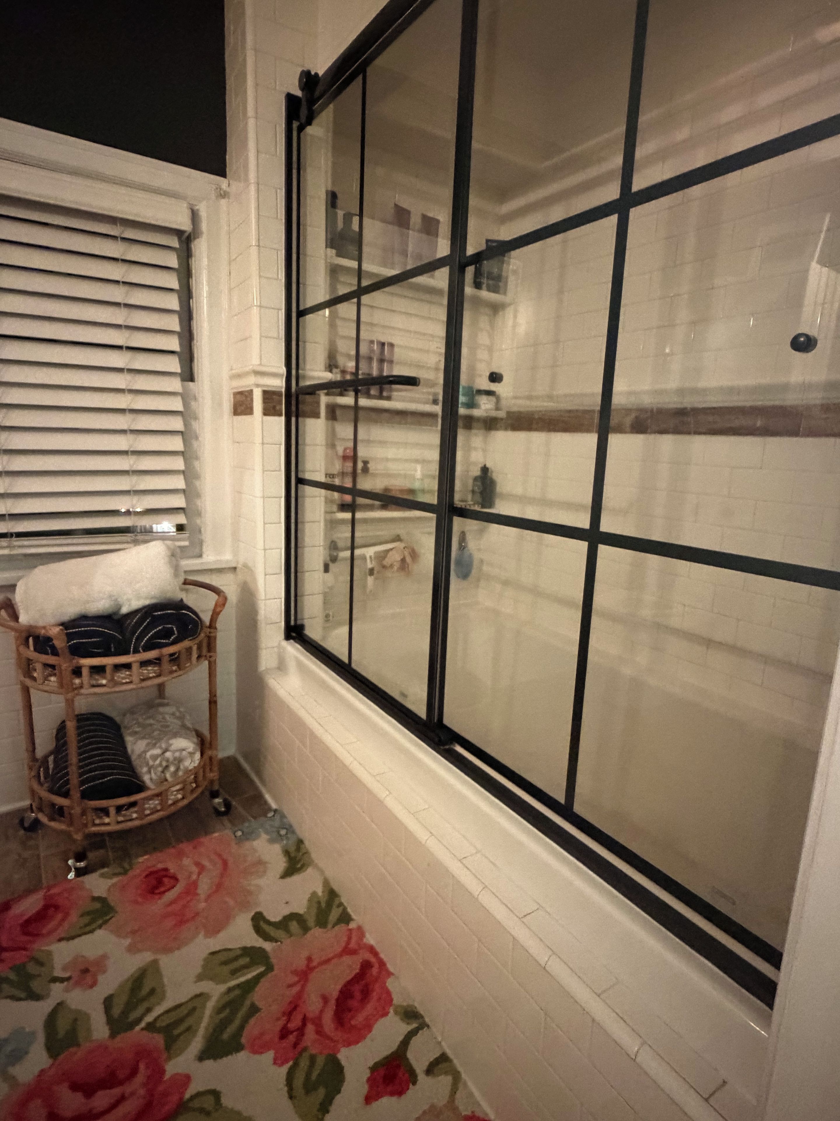 A bathroom with a glass-enclosed shower, a wicker basket with towels, and a floral-patterned floor.