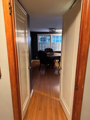 Un pasillo que conduce a un comedor con una mesa y sillas, una ventana con persianas y una puerta con picaporte de latón.