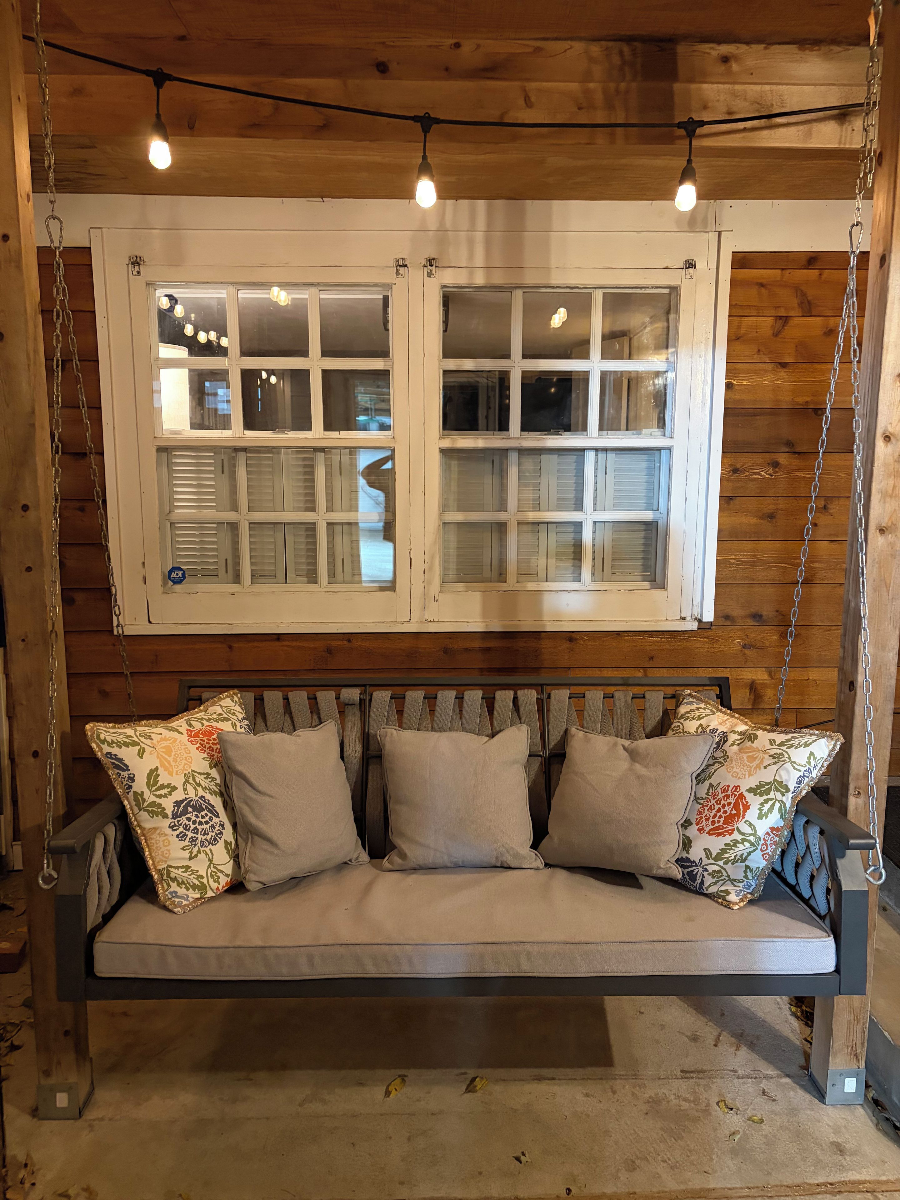 A wooden swing bed with a bench, a window with shutters, and hanging lights.