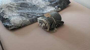 A bed with a floral-patterned pillow and a rolled-up towel.