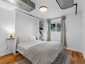 A bedroom with a bed, a bedside table with a lamp, a built-in wardrobe, a window with curtains, and a view of the outdoors. - NEW! Ridges Retreat: Pet-Friendly Stay w/Firepit (Grand Junction)