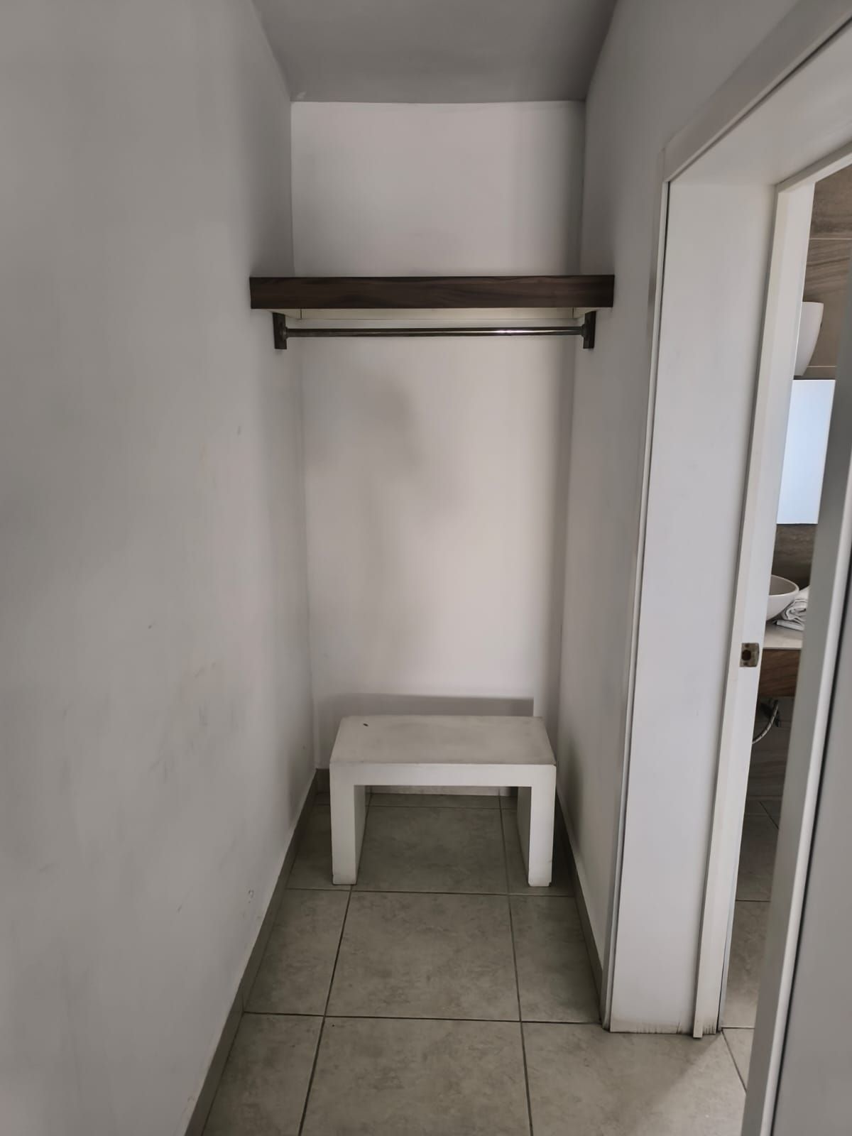 A narrow hallway with a white bench and a shelf.