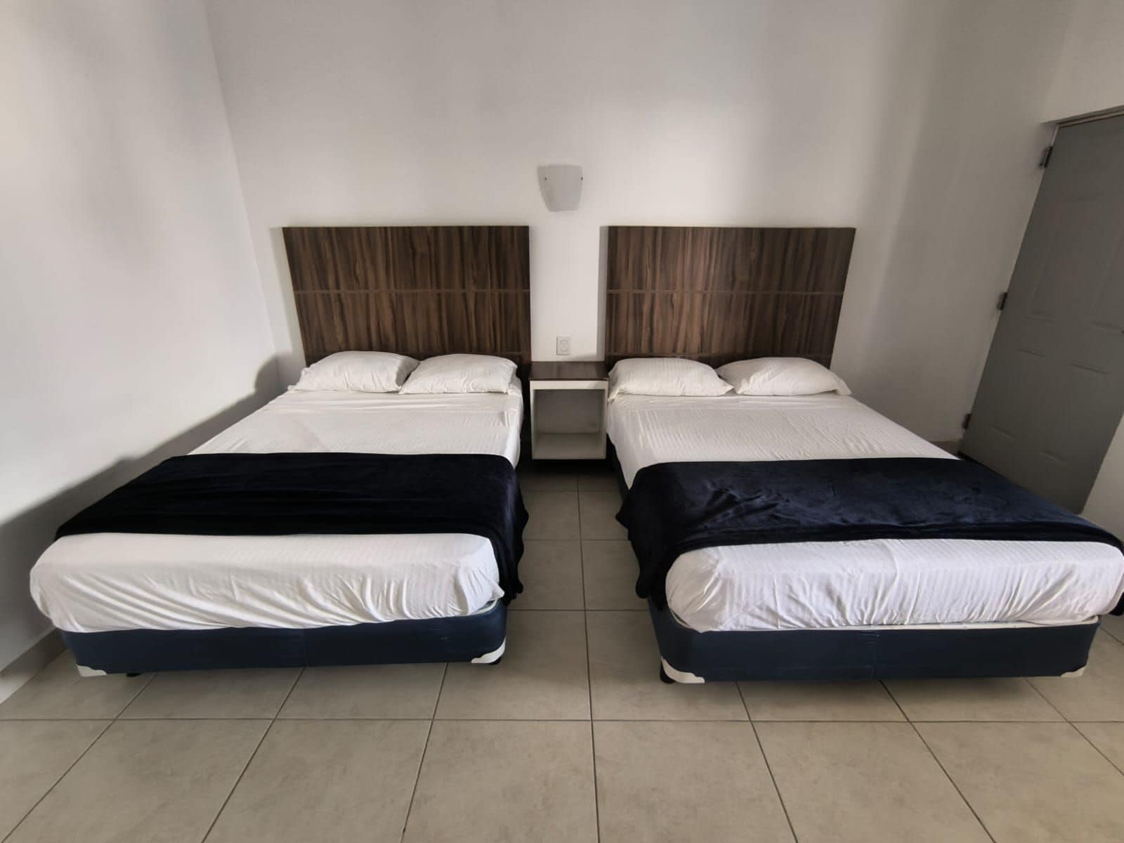 Habitación doble con dos camas, cada una con colchón blanco y cabecero oscuro.