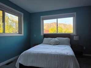 Un dormitorio con una cama, dos ventanas y una mesita de noche con una lámpara.