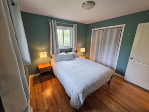 Quarto com cama, duas mesas de cabeceira, janela com cortinas e porta.