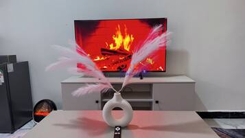 Un téléviseur à écran plat, posé sur un meuble blanc, avec un vase décoratif et des plumes sur une table devant.
