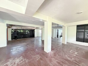 Un interior espaiós amb un sostre alt, una zona ampla oberta i una persona treballant a prop d'una porta tancada.