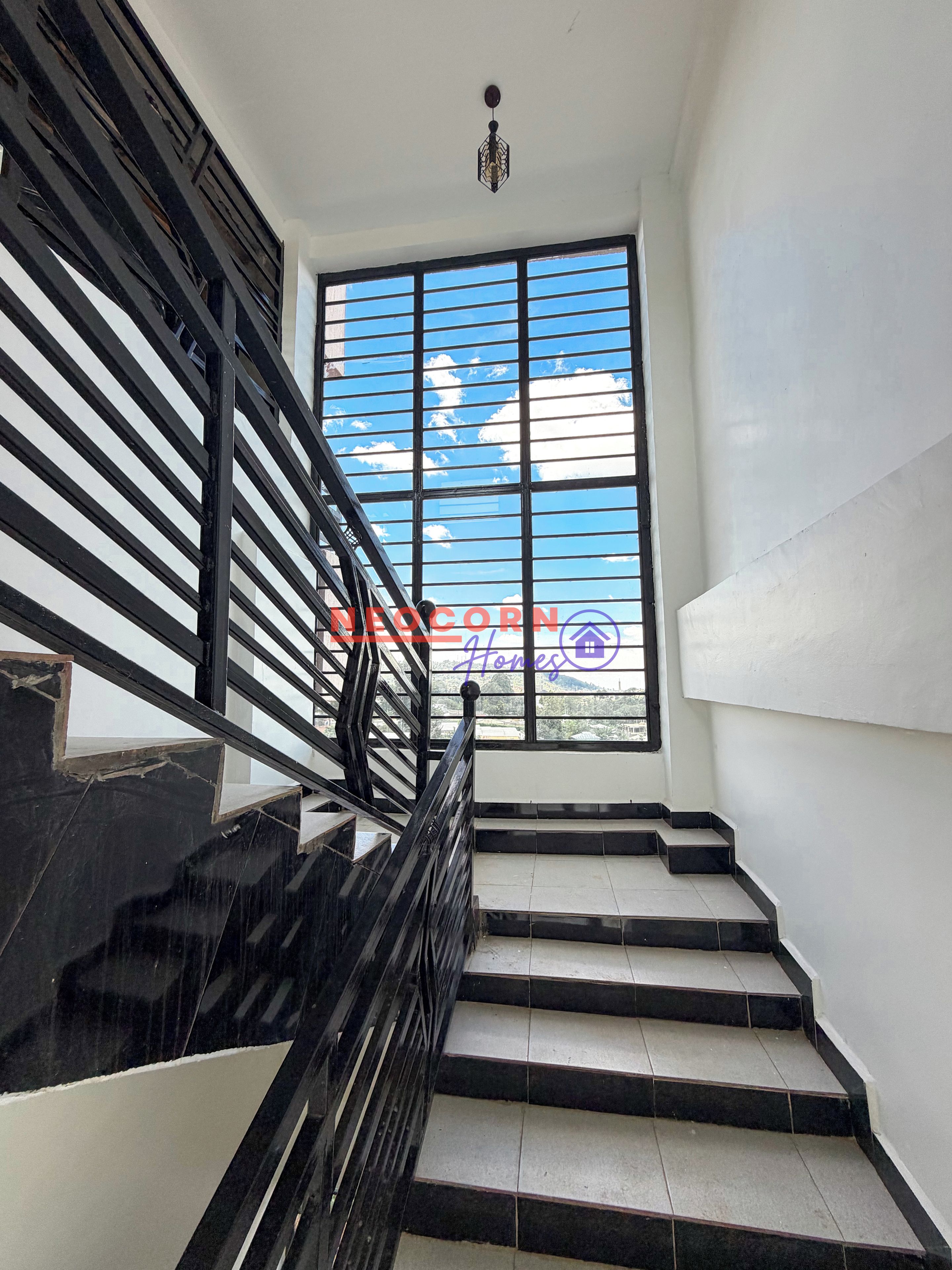 A staircase with black railings and a view of the sky through large windows.