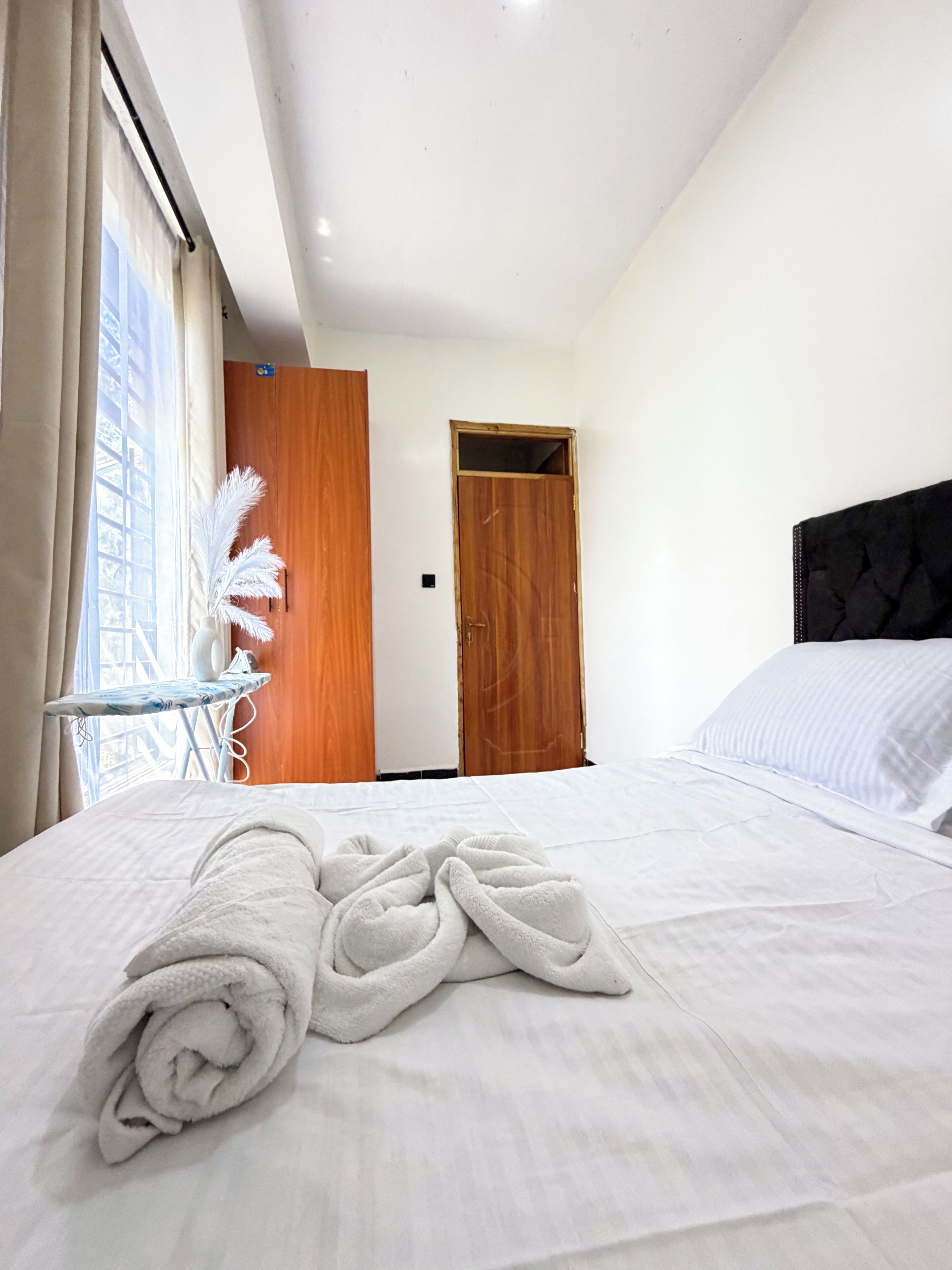 A hotel room with a neatly made bed, a wooden door, and a window with curtains.