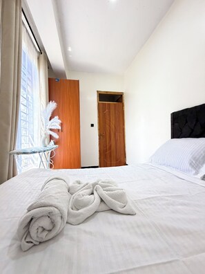 Habitació d'hotel amb un llit ben tendit, una porta de fusta i una finestra amb cortines.
