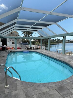 A swimming pool with a glass enclosure, surrounded by lounge chairs and a view of a body of water. - Amazing View Gulf Access 2100 Sq Ft House 3-BD Pool, Boat Lift 2 Min To Gulf Bay (Fort Myers Beach)