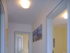 A hallway with a door leading to a room, a framed picture on the wall, and a mirror reflecting part of the hallway. - "haus Parkstrasse" - Apt. 01 (Wyk auf Foehr)