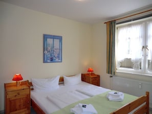A hotel room with a bed, two bedside tables with lamps, a window with curtains, and a painting on the wall. - "haus Parkstrasse" - Apt. 01 (Wyk auf Foehr)