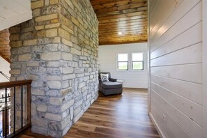 A room with a stone wall, wooden ceiling, and a gray sofa. - Mountainaire Getaway Cabin (Broken Bow)