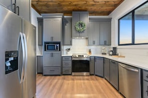 A modern kitchen with grey cabinets, stainless steel appliances, and a wooden ceiling. - Mountainaire Getaway Cabin (Broken Bow)