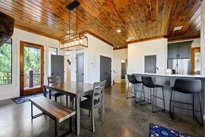 A modern kitchen with a central island, bar stools, and a dining area with a bench. - Mountainaire Getaway Cabin (Broken Bow)