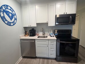 A compact kitchen with white cabinets, a stainless steel microwave, and a dishwasher. - Oceanside condo in Sea Side Villas on the beach. (Hilton Head Island)