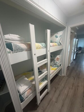 Una litera con cajones para guardar cosas, suelo de madera y un pasillo que conduce a otra habitación.