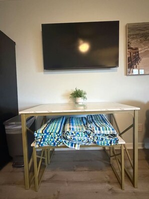 Una habitación con una televisión de pantalla plana montada en la pared, una pequeña planta en maceta sobre una mesa y una ventana con vistas a la playa.