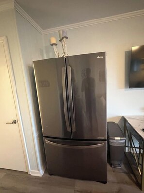 A stainless steel refrigerator in a kitchen with a marble countertop and a TV mounted on the wall. - Oceanside condo in Sea Side Villas on the beach. (Hilton Head Island)