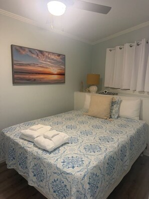 A bedroom with a bed, a painting, a lamp, and a window with curtains. - Oceanside condo in Sea Side Villas on the beach. (Hilton Head Island)