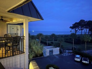 A balcony with a view of the ocean at dusk, a parking area, and a building entrance. - Oceanside condo in Sea Side Villas on the beach. (Hilton Head Island)