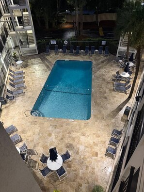 A rooftop pool area with lounge chairs and tables, surrounded by a high-rise building. - Oceanside condo in Sea Side Villas on the beach. (Hilton Head Island)