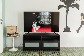 A television on a stand with a wall mural and a small table with a record player. - Salsa Paradise 1BR in Walkable Santurce (Santurce)