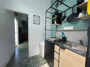 A compact kitchen with a black countertop, a sink, and a metal rack holding kitchen utensils. - Salsa Paradise 1BR in Walkable Santurce (Santurce)