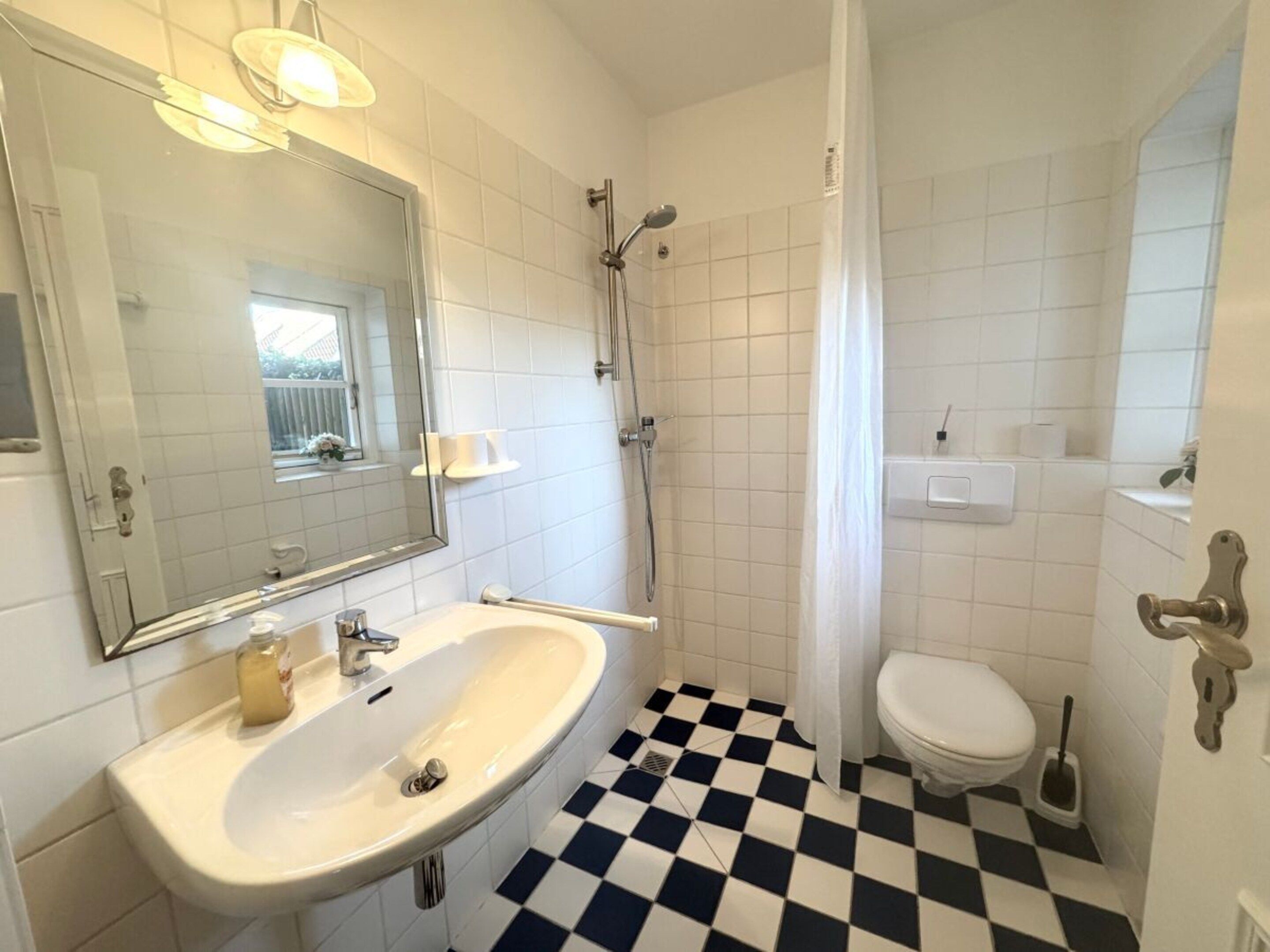 A bathroom with a white sink, a mirror, a shower, and a toilet.