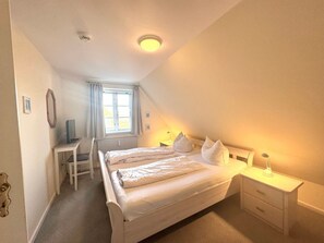 Ein Schlafzimmer mit einem Bett, Nachttischen, einem Schreibtisch und einem Fenster.