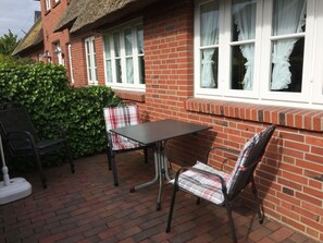 A brick house with a thatched roof, a table, and two chairs outside. - Rectory Courtyard - House Section 4 (Wrixum)