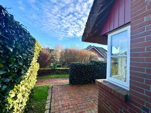 Eine Ziegelterrasse mit Hecke und blauem Himmel.