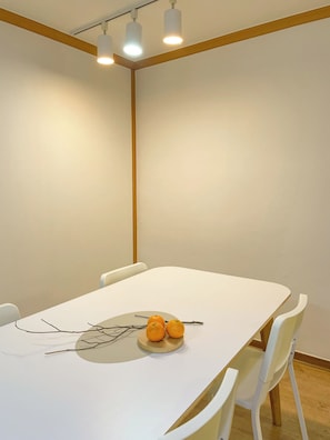 Een vergaderruimte met een witte tafel, drie stoelen en een schaal fruit met sinaasappels.