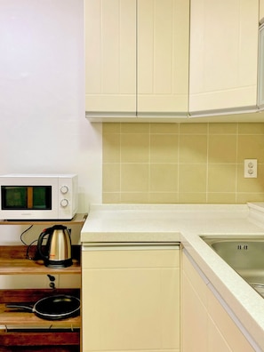 Een kleine keuken met witte kastjes, een magnetron, een waterkoker en een spoelbak.